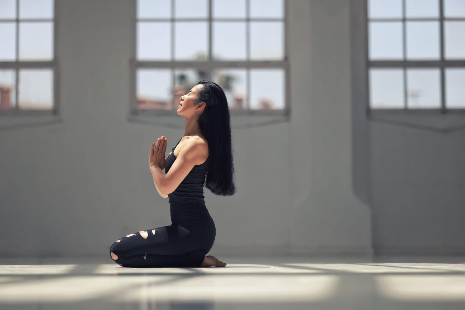 Wipa kneeling in prayer pose in a bright yoga studio